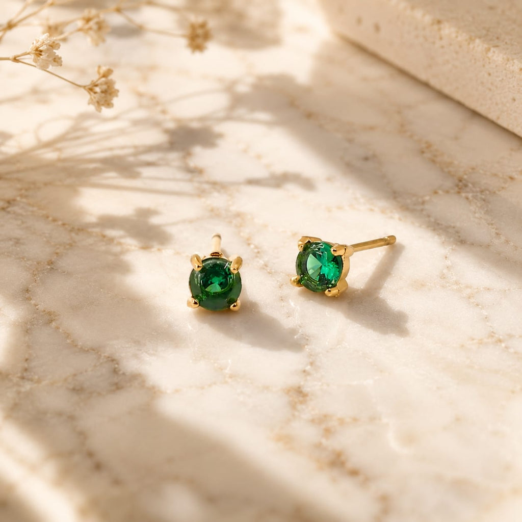 Stud σκουλαρίκια με πράσινο ζιργκόν emerald, χρυσό ανοξείδωτο ατσάλι, flat lay σε μάρμαρο — Celestial Steel