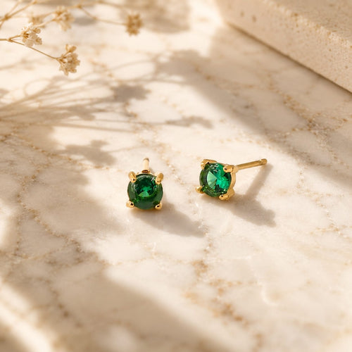 Stud σκουλαρίκια με πράσινο ζιργκόν emerald, χρυσό ανοξείδωτο ατσάλι, flat lay σε μάρμαρο — Celestial Steel