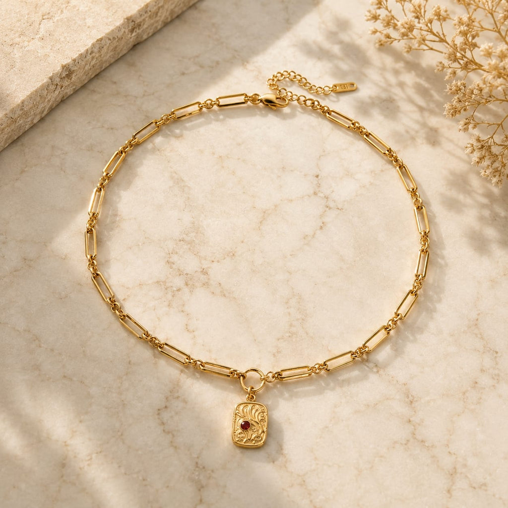 Κολιέ paperclip chain με embossed medallion charm και κόκκινη πέτρα, χρυσό ανοξείδωτο ατσάλι, flat lay σε μάρμαρο — Celestial Steel