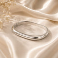 Geometric squircle bangle βραχιόλι, ασημί ανοξείδωτο ατσάλι, flat lay σε σατέν — Celestial Steel