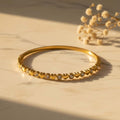 Bangle βραχιόλι με heart motifs και λευκό ζιργκόν bezel, χρυσό ανοξείδωτο ατσάλι, flat lay σε μάρμαρο — Celestial Steel