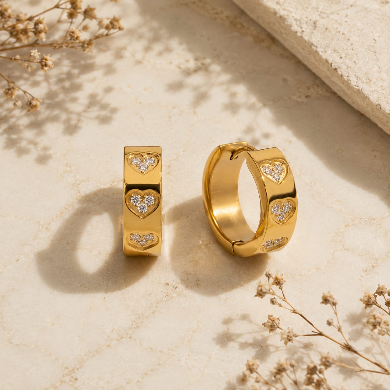 Huggie hoop σκουλαρίκια με heart motifs και λευκό ζιργκόν, χρυσό ανοξείδωτο ατσάλι, flat lay σε μάρμαρο — Celestial Steel