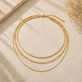 Layered 3-in-1 κολιέ herringbone, figaro και box chain, χρυσό ανοξείδωτο ατσάλι, flat lay σε μάρμαρο — Celestial Steel