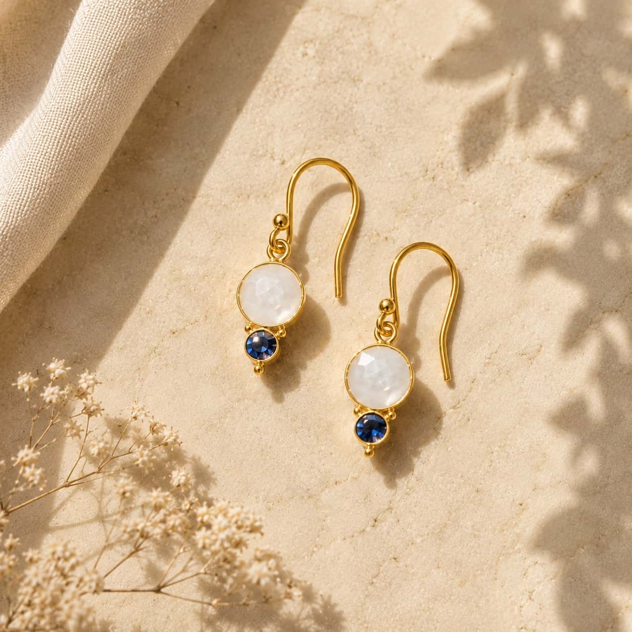 Moonstone και blue sapphire drop σκουλαρίκια, χρυσό 925 ασήμι χειροποίητο, flat lay σε μπεζ — Celestial Steel