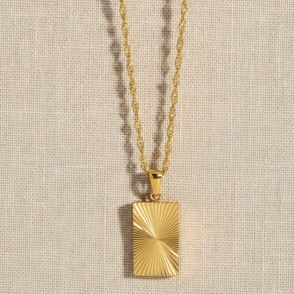 Sunburst pendant κολιέ, χρυσό ανοξείδωτο ατσάλι με sunburst engraving, flat lay σε linen — Celestial Steel