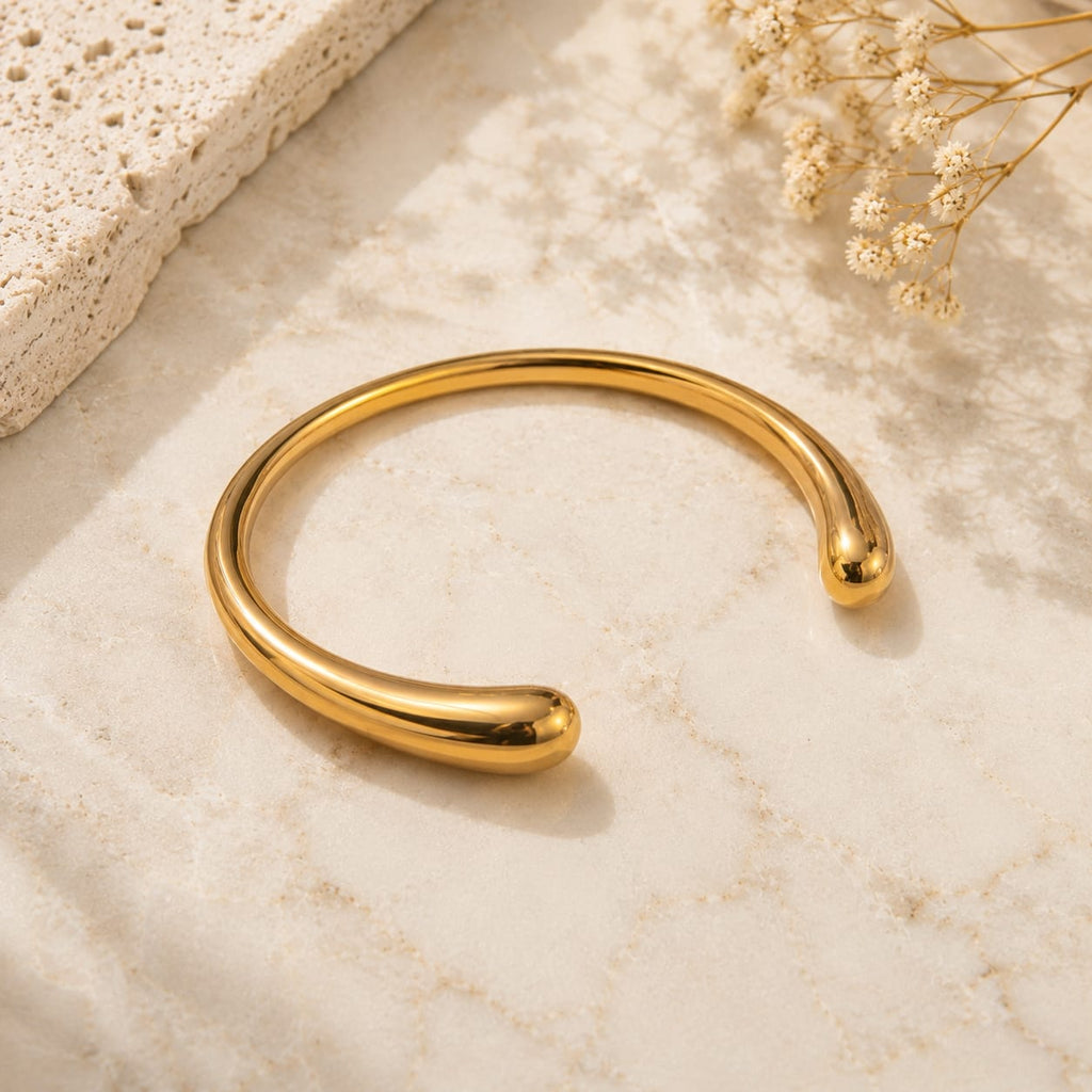Teardrop ball end open cuff bangle βραχιόλι, χρυσό ανοξείδωτο ατσάλι, flat lay σε μάρμαρο — Celestial Steel