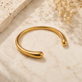 Teardrop ball end open cuff bangle βραχιόλι, χρυσό ανοξείδωτο ατσάλι, flat lay σε μάρμαρο — Celestial Steel