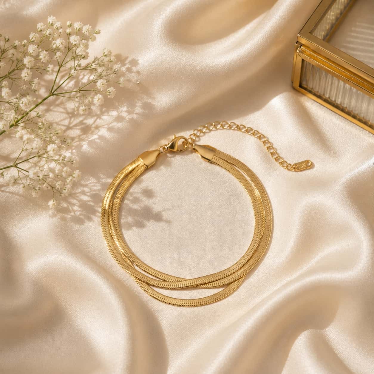 Triple herringbone βραχιόλι, χρυσό ανοξείδωτο ατσάλι, flat lay σε σατέν με glass jewelry box — Celestial Steel