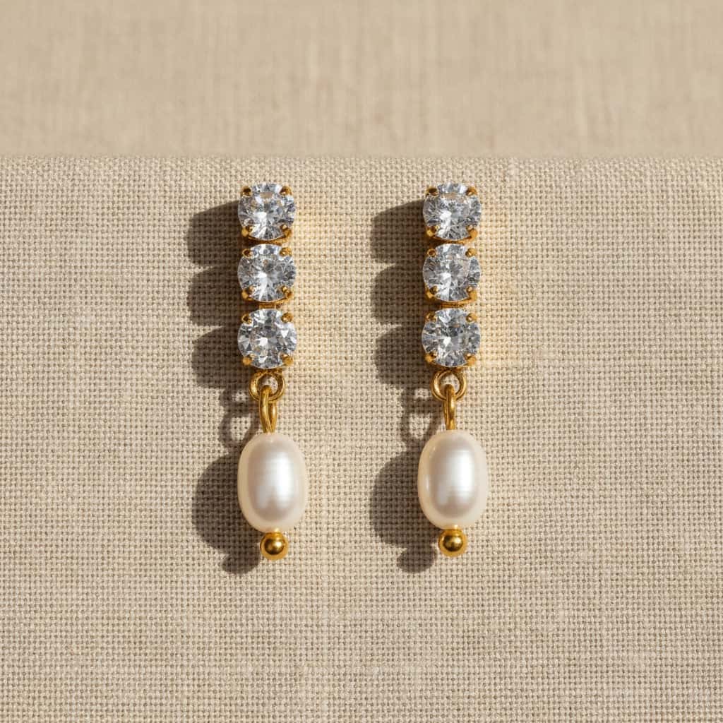 Σκουλαρίκια drop με 3 crystal ζιργκόν και freshwater pearl, χρυσό ανοξείδωτο ατσάλι, flat lay σε linen — Celestial Steel